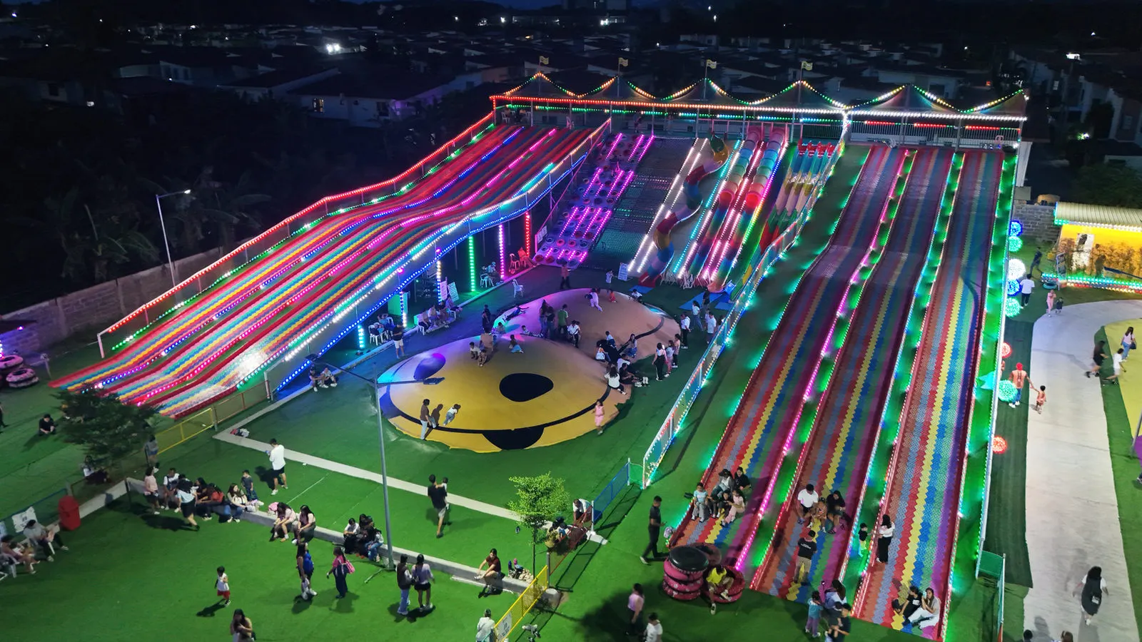 Wide rainbow-striped multi-lane slide lit at night